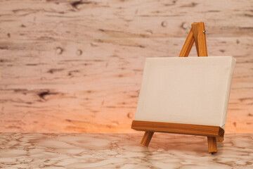 Horizontal blank canvas on wooden easel on marble surface, warm background with soft lights. Image...