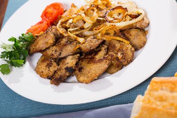 Roasted rabbit liver served with fried onion, fresh tomato and greens on white dish..