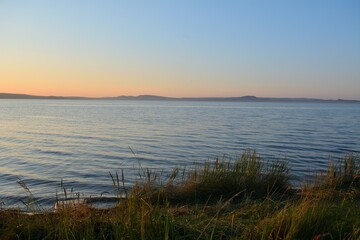 Obraz premium Reeds on the shore of a large lake surrounded by hills on a summer evening at sunset.