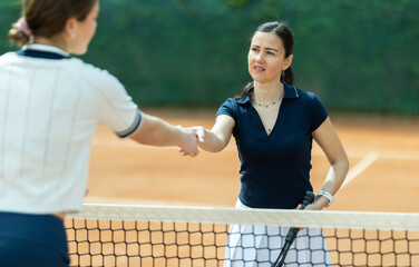 Adult woman tennis player shaking hands with her opponent on tennis court