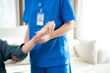 Young nurse therapy with patient while stretching muscle hand in living room at home, doctor woman...