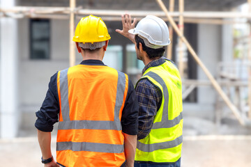 Foreman, engineer or architect with safety helmet holding laptop and blueprints for inspection details on construction in a new real estate construction site with crane and mechanical equipments.