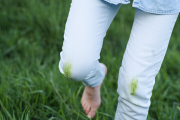 A person stands in lush green grass, showing grass stains on their white jeans. The bright sunlight...