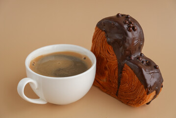 Coffee latte cappuccino drink beverage morning breakfast Heart shaped dark chocolate croissant on beige background with copy space. Puff pastry new trendy sweet dessert bakery. Creamy dough experiment