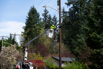 Lineman high up from truck in a lift bucket repairing the communications cable wire on a wood...