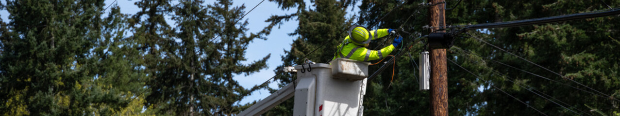 Lineman high up from truck in a lift bucket repairing the communications cable wire on a wood...