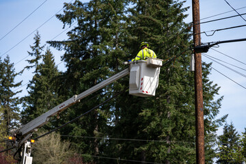 Lineman high up from truck in a lift bucket repairing the communications cable wire on a wood...