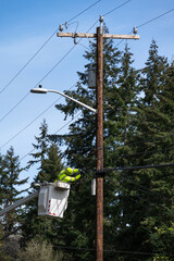 Lineman high up from truck in a lift bucket repairing the communications cable wire on a wood...