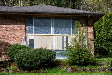 Older brick house with weathered wood siding, painted with sample colors, and windows covered with plastic in preparation for painting project
