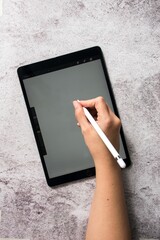 Person using a stylus on a digital tablet on a textured surface, showcasing modern technology use