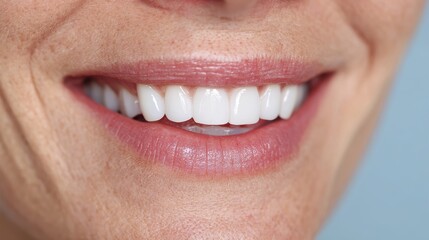 Fototapeta premium Smiling woman with healthy teeth and gentle smile, indoors with plain blue background, cropped close-up.