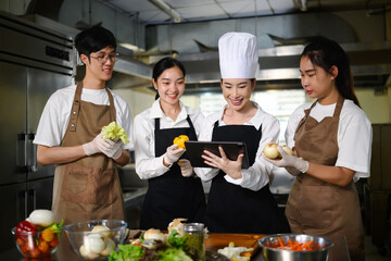 Smiling chef teacher using a tablet to explain a recipe to students in a professional kitchen