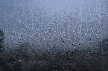 Raindrops on a glass window with a blurry cityscape in the background on a cloudy day.