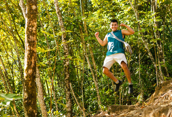 Young backpacker jumping happily in the Colombian jungle during his vacation, showing a lot of energy and vitality