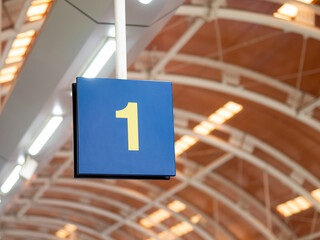Hanging blue sign with yellow number 1 at a transportation terminal, captured beneath a curved roof...
