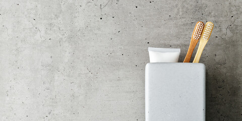 Aesthetic Beige bamboo toothbrushes and toothpaste in toothbrush holder in grey bathroom, concrete background copyspace. Simplicity, hygiene, environmentally friendly alternatives, copyspace