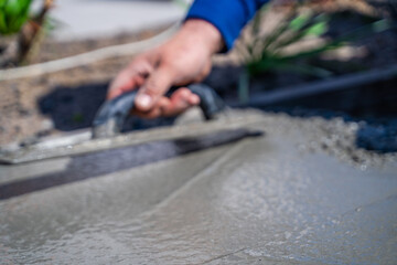 A man's hand is leveling freshly poured cement with a trowel, close-up