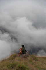 Hiker man enjoying beautiful sunrise in morning mountains. Traveler on mountain with white fog below.