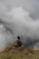 Hiker man enjoying beautiful sunrise in morning mountains. Traveler on mountain with white fog below.