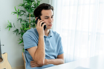 Asian upset depressed man talking on mobile phone in living room at home. 