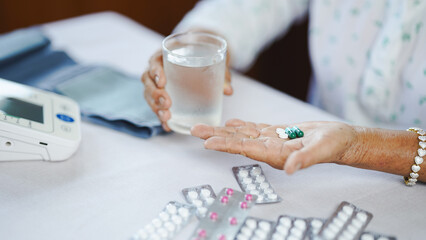 Elderly person holding pills and glass of water, medication and healthcare concept, close up view