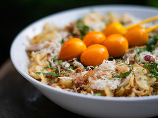 Close-up of Indonesian chicken porridge (bubur ayam) topped with shredded chicken, fried shallots, herbs, and skewered golden egg yolks, served in a white bowl.