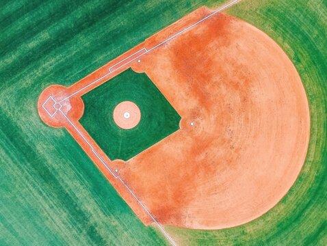 Aerial view of a baseball field showing home plate and infield in vibrant green and orange colors from above - Powered by Adobe