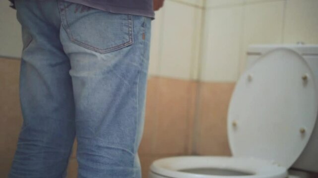 Stomach ache, sick asian young man holding stomach pain and holding tissue paper roll in bathroom, standing near toilet, boy suffer from diarrhea his stomach painful. Hygiene, health care concept.