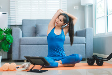 Young Asian woman practices yoga by stretching her back on a yoga mat in the living room at home....