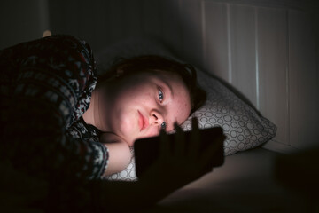 Girl using smart phone while lying on bed in bedroom