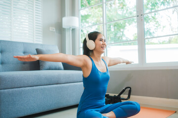 Young Asian woman practices yoga by stretching her back on a yoga mat in the living room at home....