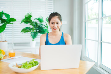 Beautiful Asian woman in fitness sportswear happily smiles while slicing vegetables and fruits on...