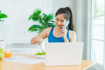 Beautiful Asian woman in fitness sportswear happily smiles while slicing vegetables and fruits on...
