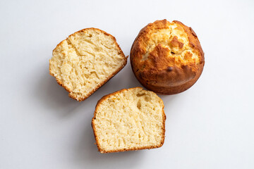 Two muffins on a white surface, one cut in half. The muffins are golden brown and have a slightly crispy texture. Homemade baking and pastry made from wheat flour. Making bread and Easter cakes