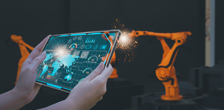 Industry engineer in smart factory using transparent glass tablet to control automated robotic arm with AI and 5G network, machine learning technology, business innovation in industry 4.0 era