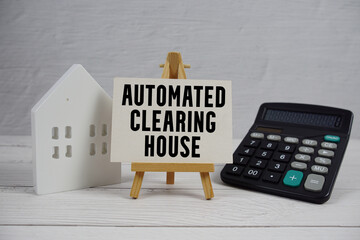 ACH Automated Clearing House text on paper card with white house model and calculator on wooden background