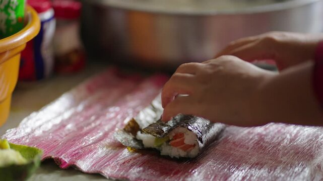Chef carefully lays sliced fish over rice as part of sushi roll assembly in kitchen scene, forms and rolls carefully