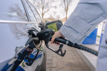 A person fuels a black diesel vehicle at a station, holding the nozzle firmly in the car’s tank...