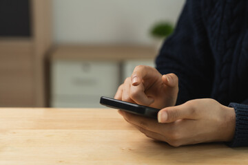 Person Using Smartphone at a Wooden Table, Focusing on Mobile Device with Hands in a Casual Indoor Environment