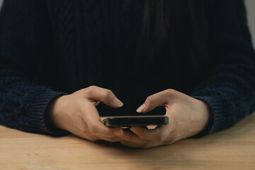 Close-up of Person Holding Smartphone in Hands While Sitting at a Wooden Table with Dark Sweater, Focus on Mobile Device and Fingers