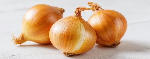 Three whole yellow onions rest on a light wooden surface, showcasing their golden-brown skins and natural texture.