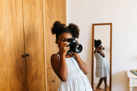 Creative afro-haired girl photographing a moment at home with a digital camera
