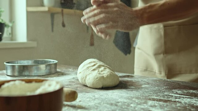 A baker in an apron kneads the dough with his hands and sprinkles it with flour to bake delicious homemade bread.