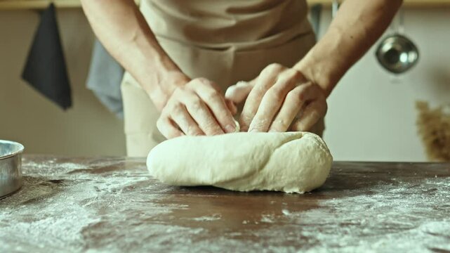 A baker in an apron kneads the dough with his hands and sprinkles it with flour to bake delicious homemade bread.