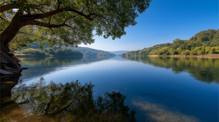 Fototapeta premium Serene lake under blue sky with lush greenery and sunlight reflections