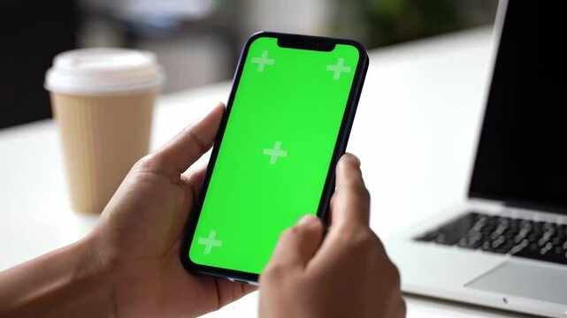 Close-Up of Hands Holding Smartphone with Green Screen in Modern Workspace
