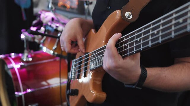 Bass guitarist bassist plays bass guitar during performance at party, concert. Close-up, hands of bass guitarist professionally play pop or rock music on electric bass guitar. Concert lighting