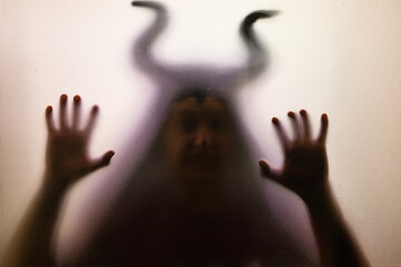 Horror, halloween background - Shadowy figure with horns behind the glass