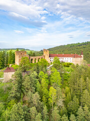 Fototapeta premium An aerial view reveals Velhartice Castle nestled in lush greenery, showcasing its majestic walls and surrounding forests during a clear day.