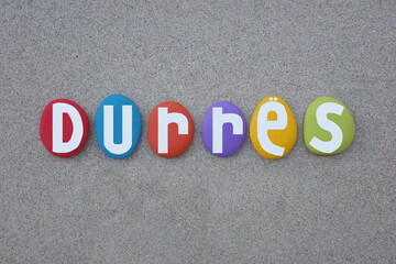 Durres, city of Albania, creative logo composed with multi colored hand painted stone letters over beach sand